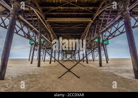 Unter dem Lytham St Annes Pier an der küste von lancashire. Symmetrie in den alten Metallsäulen und Kabeln. Stockfoto