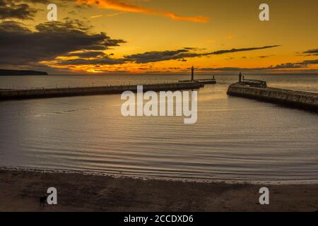 Sonnenuntergang über Whitby Hafen mit eingehender Flut. Warmer Himmel und sanfte Wellen, die sich am Strand waschen Stockfoto