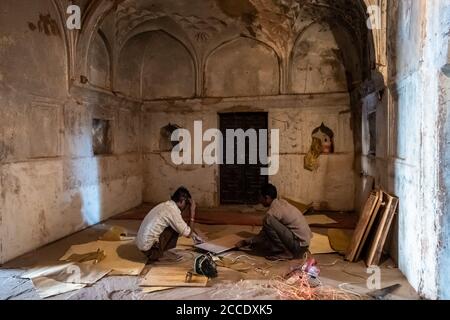 Orchha, Madhya Pradesh, Indien - März 2019: Zimmerleute, die Restaurierungsarbeiten innerhalb einer dunklen Halle des Jehangir Mahal Palastes im Orchha Fort tun. Stockfoto