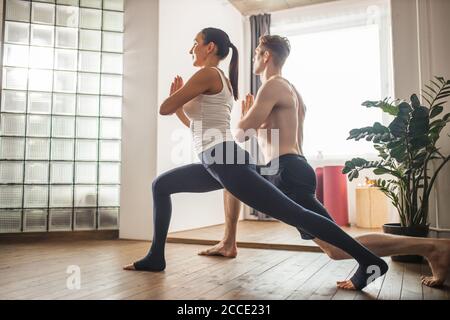 Junge kaukasische Paar tut Fitness-Training zu Hause. Gemeinsam Yoga üben. Verheiratetes Paar Kniebeugen, stehen in einer Pose. Gesunder Lebensstil conce Stockfoto