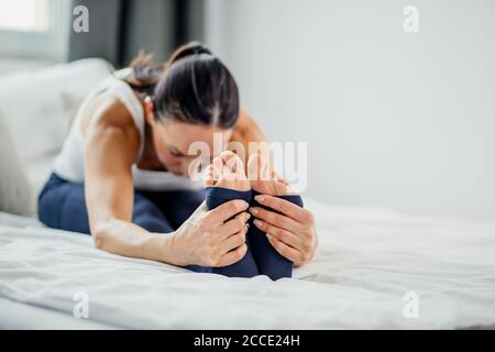 Schlanke kaukasische sportliche Frau macht Übungen auf dem Bett zu Hause, junge Dame Stretching am Morgen, gesunde Lebensweise Konzept Stockfoto