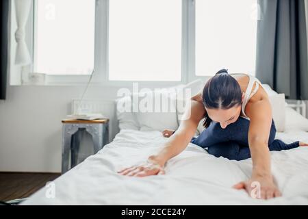 Schlanke kaukasische sportliche Frau macht Übungen auf dem Bett zu Hause, junge Dame Stretching am Morgen, gesunde Lebensweise Konzept Stockfoto