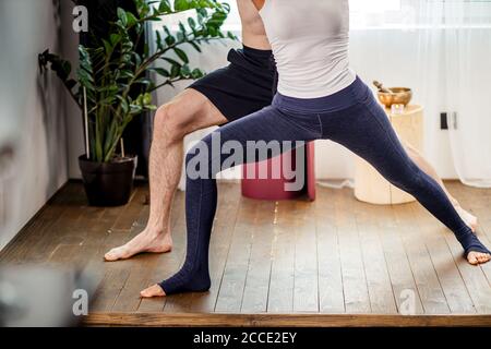 Cropped Foto von starken flexiblen Mann lehren seine Freundin, die richtige Position in Yoga zu nehmen, Paar Übungen zu Hause, trägt Sportbekleidung. Isolate Stockfoto