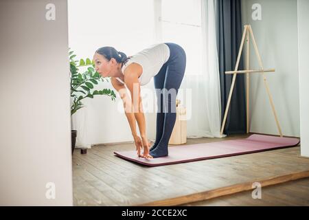 Junge kaukasische sportliche Fitness-Frau macht Übungen, Stretching zu Hause, attraktive Dame in Sportkleidung führt gesunde Lebensweise. Drinnen Stockfoto