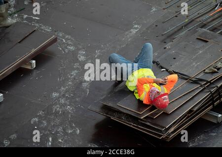 Austin, TX USA 25. Juli 2020: Betonbesatzungsmitglied schaut auf sein Handy, während er eine Pause macht, nachdem er in der Parkgarage eines 53-stöckigen Gebäudes während eines nächtlichen Gepierens in der Innenstadt von Austin, TX, gearbeitet hat. Trotz der landesweiten COVID-19-Pandemie und des Staates, der mit über einer halben Million Fällen und über 10,000 Todesfällen heimgesucht wird, werden in Texas weiterhin riesige Bauprojekte unvermindert durchgeführt. Stockfoto