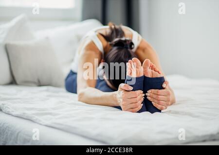 Sportlich attraktive Dame Stretching Beine auf dem Bett zu Hause, Frau machen Übungen am Morgen Stockfoto