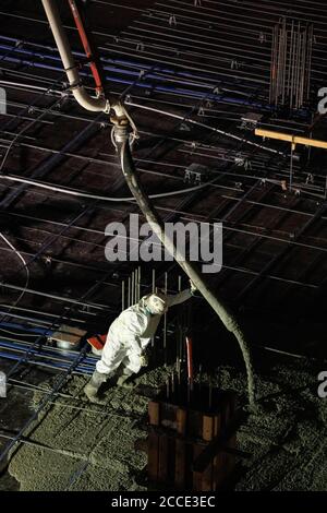 Austin, TX USA 25. Juli 2020: Gepumpter Beton fließt durch eine Röhre auf den Boden einer Parkgarage, die Teil eines 53-stöckigen Gebäudes im Bau ist, während eines nächtlichen Zuflutes in der Nähe der Innenstadt von Austin. Stockfoto