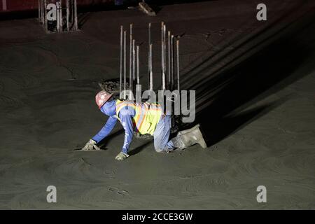 Austin, TX USA 25. Juli 2020: Betonarbeiter nutzt eine Handkelle, um Beton auf der Parkgarage eines 53-stöckigen Gebäudes während eines nächtlichen Gefalles in der Innenstadt von Austin, TX, zu glätten. Trotz der landesweiten COVID-19-Pandemie und des Staates, der mit über einer halben Million Fällen und über 10,000 Todesfällen heimgesucht wird, werden in Texas weiterhin riesige Bauprojekte unvermindert durchgeführt. Stockfoto