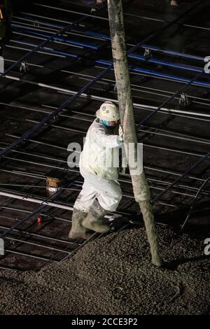 Austin, TX USA 25. Juli 2020: Gepumpter Beton fließt durch eine Röhre auf den Boden einer Parkgarage, die Teil eines 53-stöckigen Gebäudes im Bau ist, während eines nächtlichen Zuflutes in der Nähe der Innenstadt von Austin. Stockfoto