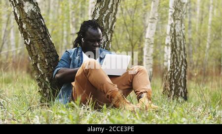 Neuer Normalwert. Remote-Work-Konzept. Afrikanischer Mann mit Laptop in der Natur. Hochwertige Fotos Stockfoto