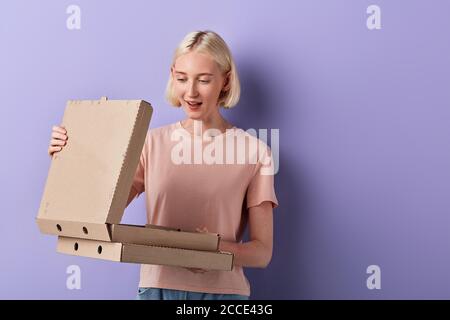 Happy blonde Mädchen hält heiße Pizza in der Box, isoliert auf violett, Frau gehen, um Fast Food zu essen. Nahaufnahme Porträt, Studio erschossen. Lieferung Stockfoto