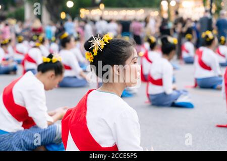 Chiang Mai, Thailand, 10. November 2019: Gruppe junger Frauen in traditionellen Thai-Kleidern und einem roten Band und Blumen im Kopf auf dem Boden sitzend Stockfoto