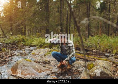Junge müde Wanderer Trinkwasser aus einem reinen Bergbach, voller Länge Foto.Lifestyle, Freizeit, Freizeit Stockfoto