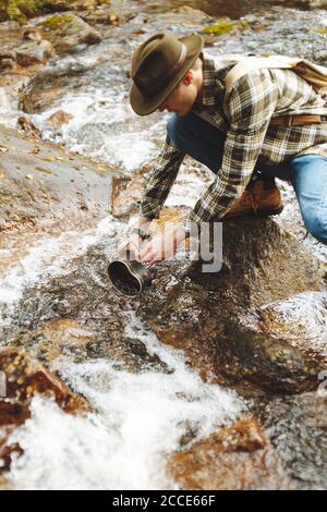 Junger Mann im karierten Hemd. Jeans bekommen Wasser aus dem Bach, Nahaufnahme beschnitten Foto. Stockfoto