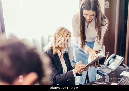 Freundliche blonde weibliche Chief Executive Unterzeichnung Dokument und hören ihre Kollegin Bericht, in ihrem Büro. Business, Multitasking-Konzept Stockfoto