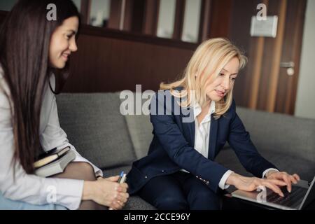 Brunette Mädchen Anordnung Treffen mit weiblichen Tieflyer oder Steuerberater im Büro. Blonde Steuerberater Beratung Client beim Zeigen auf Laptop-Bildschirm. Stockfoto