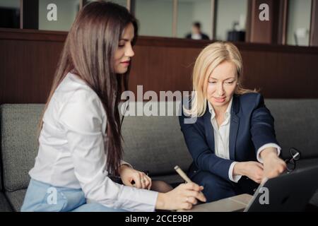 Brunette Mädchen Anordnung Treffen mit weiblichen Tieflyer oder Steuerberater im Büro. Blonde Steuerberater Beratung Client beim Zeigen auf Laptop-Bildschirm. Stockfoto