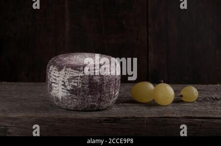 Nahaufnahme von weichem französischem Käse mit violetter Kruste und Drei Trauben auf dem Holzteller Stockfoto