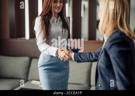 Zwei kaukasische Geschäftsfrauen in Bürokleidung, die beim Treffen die Hände schütteln, während sie eine Partnerschaft schließen, konzentrieren sich auf die Hände Stockfoto