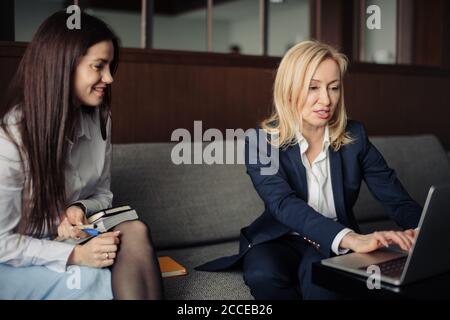 Brunette Mädchen Anordnung Treffen mit weiblichen Tieflyer oder Steuerberater im Büro. Blonde Steuerberater Beratung Client beim Zeigen auf Laptop-Bildschirm. Stockfoto