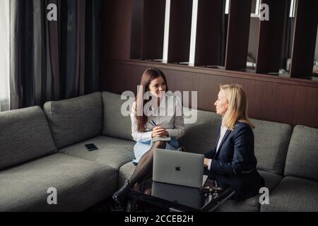 Brunette Mädchen Anordnung Treffen mit weiblichen Tieflyer oder Steuerberater im Büro. Blonde Steuerberater Beratung Client beim Zeigen auf Laptop-Bildschirm. Stockfoto