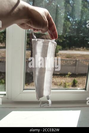 Weibliche Hand hält zwei Masken vor dem Fenster. Vor dem Fenster ist ein sonniger Tag und gutes Wetter. Isolierung. Isolationskonzept. Konzentrieren Sie sich auf den ma Stockfoto