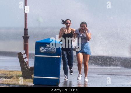 Zwei junge weiße Weibchen, die während der starken Winde des Sturms Ellen in Southend on Sea, Essex, Großbritannien, durch krachende Wellen Rennen, werden nass und durchnässt Stockfoto