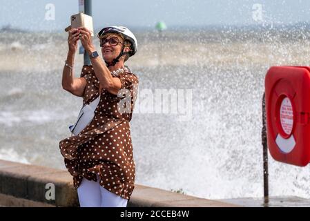 Weiße kaukasische Frau, die während der starken Winde des Sturms Ellen ein Selfie in Southend on Sea, Essex, UK, mit krachenden Wellen und Rettungsgurt macht Stockfoto