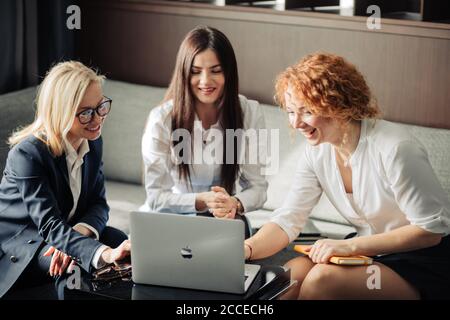 Rothaarige weibliche korporative Mentorin, die zwei jungen weiblichen Angestellten bei der Computerarbeit im Freiraum-Büro hilft, nah oben. Stockfoto