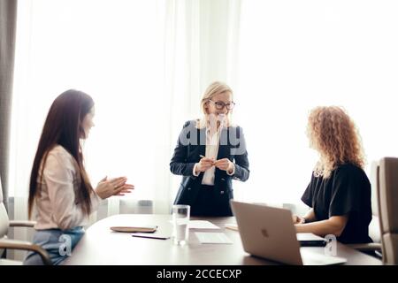 Weibliche Marketing-Experten sitzen um den Tisch und betrachten eine Sprecherin bei einem informellen Treffen. Blonde kaukasische weibliche Führungskraft, die eine Presentatio Stockfoto