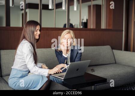 Zwei elegante klassische Business-Frauen, weibliche Partner in formeller Kleidung mit Gespräch, Planung Projektbudget während sitzen auf Couch im Büro Stockfoto