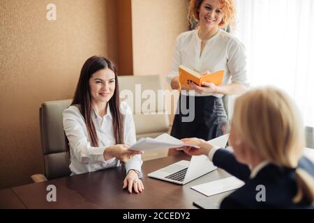 Zwei junge freundlich aussehende weibliche Rekrutierer hören Brünette Kandidat während des Vorstellungsgesprächs im Büro. Stockfoto