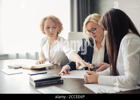 Weibliche Business-Team von jungen attraktiven Mitarbeitern diskutieren Online-Projekt in modernen Büro, Zusammenarbeit mit Notizblöcken für Notizen. Stockfoto