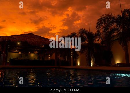 Schöner orange feuriger Sonnenuntergang in den Tropen. Straßendach von Heu, neben dem Pool und mit Blick auf das Reisfeld Stockfoto