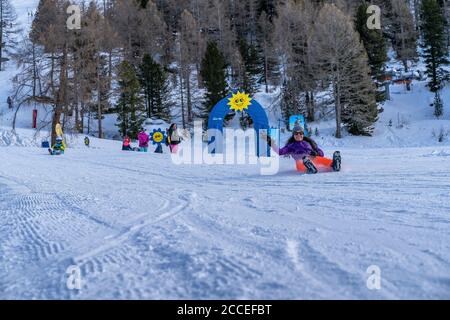 Europa, Schweiz, Wallis, Grächen, Hannigalp, junge Frau hat Spaß beim Rutschen mit einer Schneeplatte Stockfoto