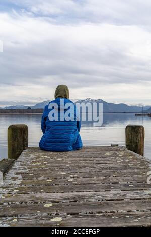 Europa, Deutschland, Bayern, Rosenheim, Prien am Chiemsee, Chiemsee, Mann sitzt auf dem Steg und blickt über den Chiemsee zu den Chiemgauer Alpen Stockfoto