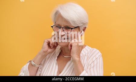 Porträt einer alten Frau, die Musik mit kabellosen Kopfhörern hört, isoliert auf orangefarbenem Hintergrund. Hochwertige Fotos Stockfoto