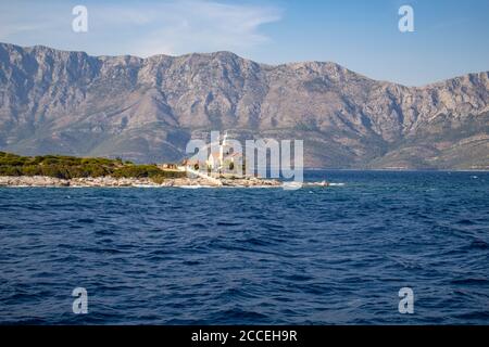 Sucuraj/Kroatien - 3. August 2020: Leuchtturm am Rande der Insel Hvar mit dem mächtigen Biokovo-Berg, der im Hintergrund auf Kroatien aufragt Stockfoto