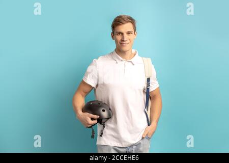 Porträt des jungen kaukasischen Mann in weißen T-Shirt hält sportliche Helm für Motorrad in den Händen und Lächeln, isoliert auf blauem Hintergrund. Sport, Fahrrad Stockfoto