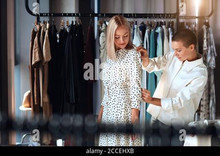 Moderne kaukasische Designerin nimmt gerne Messungen von jungen Frauen im Zimmer. Hintergrundkleidung Stockfoto