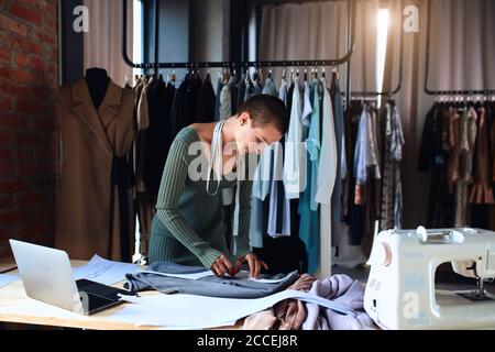 Weibliche Schneiderin nähen neue Kleidung im Studio mit Laptop Stockfoto