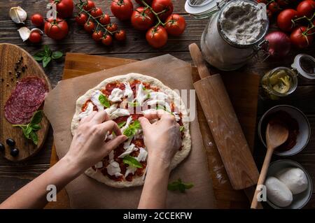 Eine Frau bereitet eine Pizza zu, knetet den Teig und legt Zutaten auf den Küchentisch. Dunkel und launisch, Luftaufnahme. Stockfoto