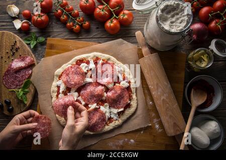 Eine Frau bereitet eine Pizza zu, knetet den Teig und legt Zutaten auf den Küchentisch. Dunkel und launisch, Luftaufnahme. Stockfoto