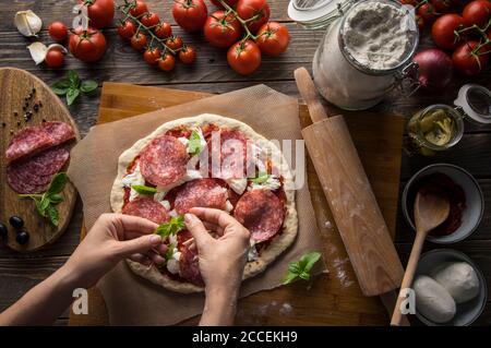 Eine Frau bereitet eine Pizza zu, knetet den Teig und legt Zutaten auf den Küchentisch. Dunkel und launisch, Luftaufnahme. Stockfoto