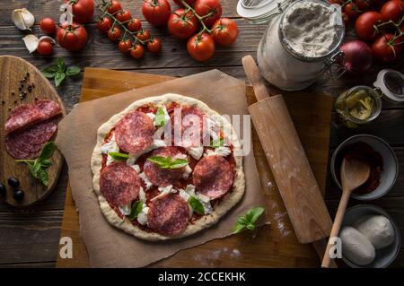 Eine Frau bereitet eine Pizza zu, knetet den Teig und legt Zutaten auf den Küchentisch. Dunkel und launisch, Luftaufnahme. Stockfoto