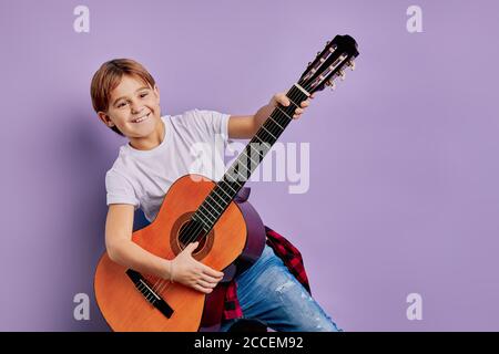 Portrait von schönen fröhlichen Kind auf der Gitarre spielen, Musik isoliert über lila Hintergrund Stockfoto