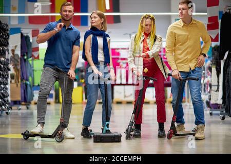 Gruppe von glücklichen kaukasischen Freunden auf Skallermann im Sportartikelgeschäft, gutaussehende Jungs und schöne Frauen haben Spaß beim Einkaufen, im Sport engagiert Stockfoto