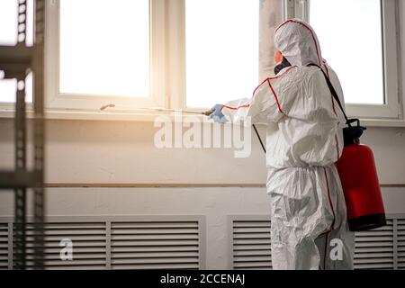 Professionelle kaukasische Desinfektionsmittel Entfernen von Infektionen Coronavirus covid-19 von Oberflächen. Männlich in Schutzanzug verwenden spezielle Ausrüstung Sprays zu kil Stockfoto