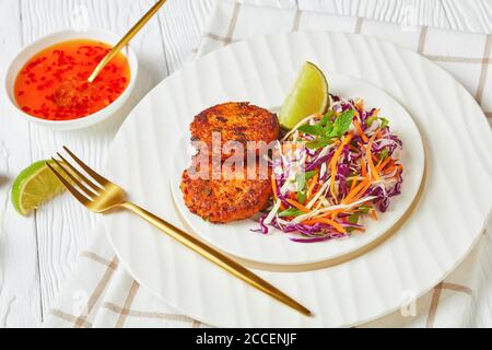 Gebratene thai-Fischkuchen mit Krautsalat auf einem Teller auf einem Holztisch mit süßer Chilisauce, horizontale Ansicht von oben, Nahaufnahme Stockfoto