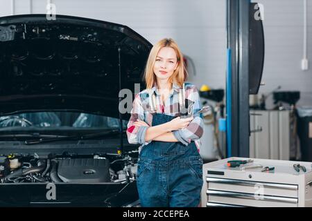 Angenehme attraktive blonde selbstbewusste Mechaniker stehen vor dem kaputten Auto, Nahaufnahme Porträt. Hobby, Beruf Stockfoto